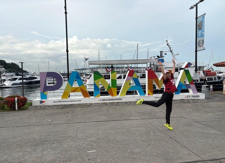 A person jumping in front of a colorful sign that spells 'PANAMA' with a marina and boats in the background. 2