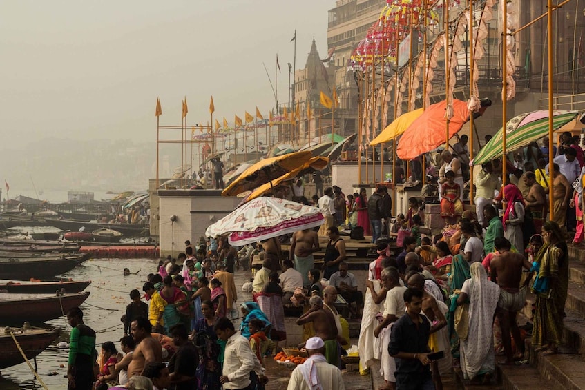 A crowded riverside with people, boats, and colorful umbrellas. 3