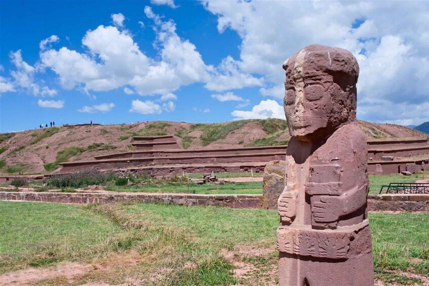 A large stone statue in a grassy field with a clear sky and distant hills. 1