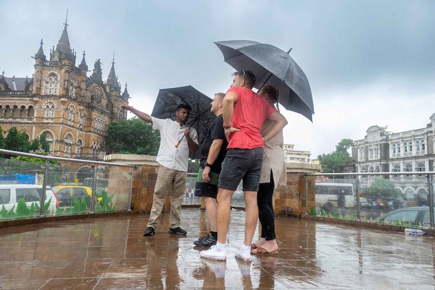 A group of people standing on a wet terrace with a historic building in the background. 1