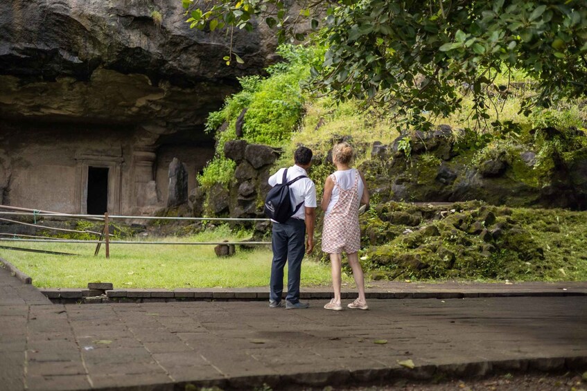 A couple standing by a cave entrance with a rocky overhang and greenery. 5
