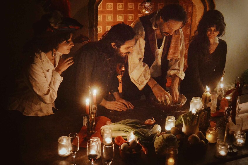 A group of people gathered around a table with candles and food, in a dimly lit setting. 1