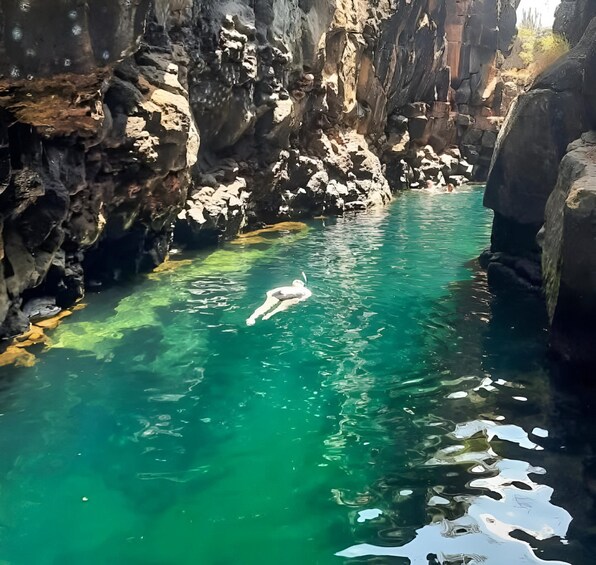 A person swimming in a clear turquoise pool surrounded by rocky cliffs. 1