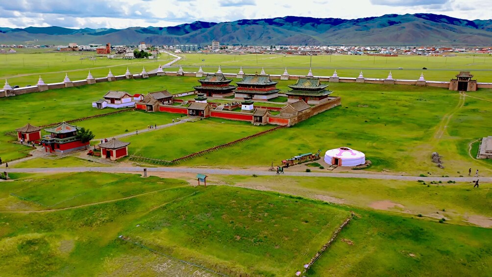 A traditional yurt surrounded by a fortified compound with multiple buildings, including a red-roofed structure and a white pagoda. 4