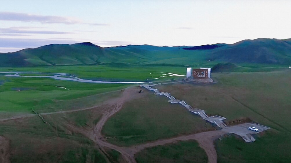 A rural landscape with a winding road, a small building, and rolling hills. 2