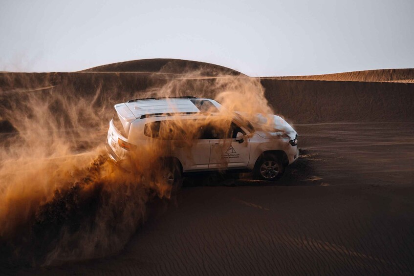 A white SUV driving through a sandy desert with dust being kicked up. 1