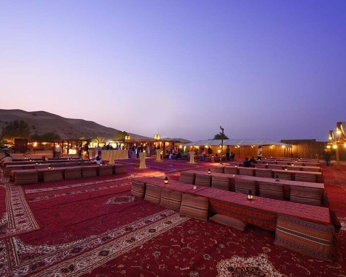 An outdoor seating area with patterned rugs and benches, under a clear sky. 2