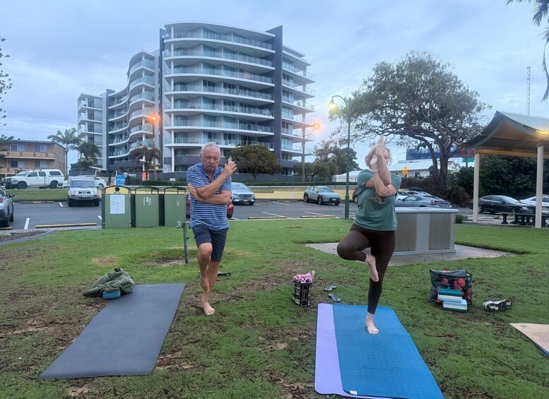 Two people exercising on outdoor mats in a park with buildings in the background. 5