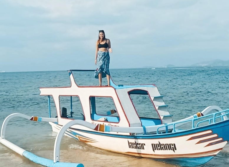 A person standing on a boat with the text 'laskar pelangi' on its side. 5