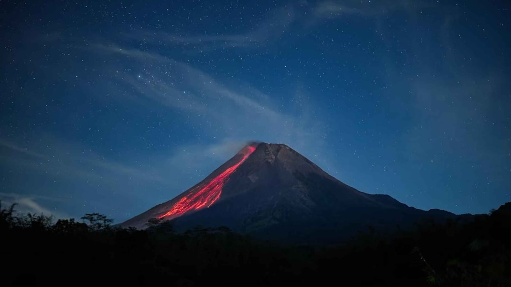 A mountain with a glowing red lava flow at its peak under a starry night sky. 3