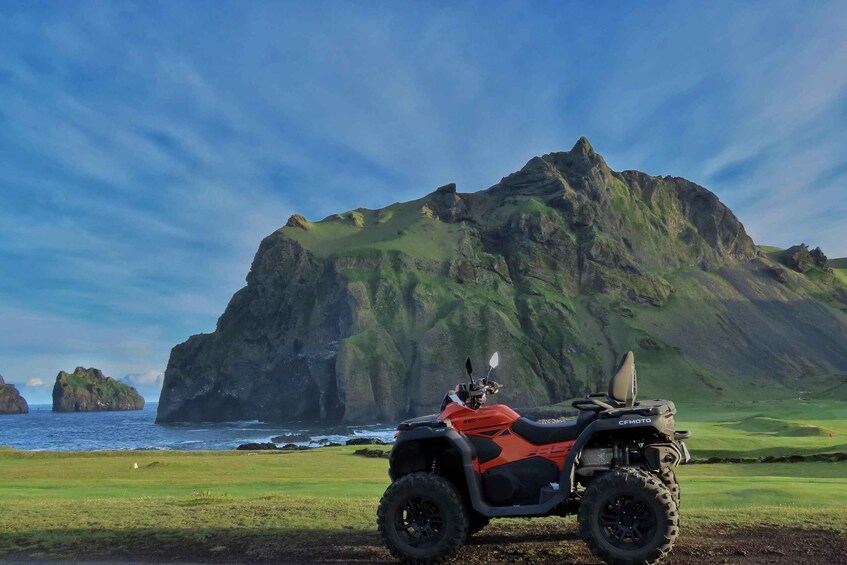 An orange ATV parked on a grassy field with a mountainous landscape in the background. 5