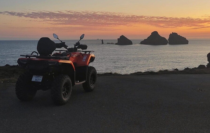 An ATV parked on a road with a sunset and rocky formations in the background. 3