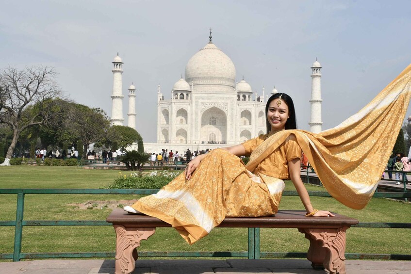 A person sitting on a bench with the Taj Mahal in the background. 2