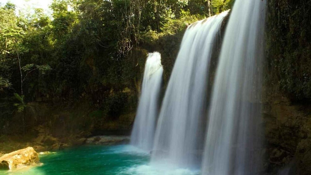A waterfall cascading into a turquoise pool surrounded by dense forest. 1