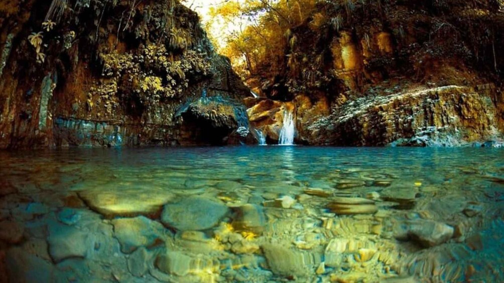 A cave with a waterfall and clear water. 4