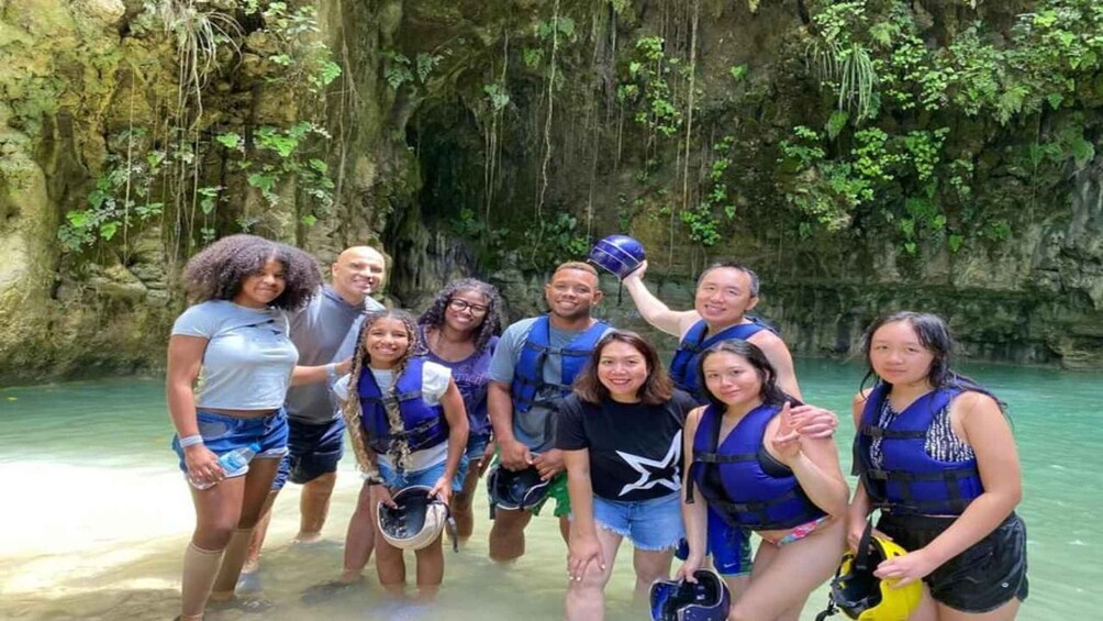 A group of people in a natural setting with a rocky cliff and greenery in the background. 5