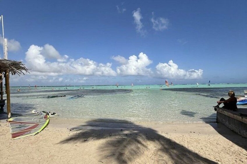 Una playa con aguas turquesas cristalinas, una palmera y una persona sentada en un borde de hormigón. 3
