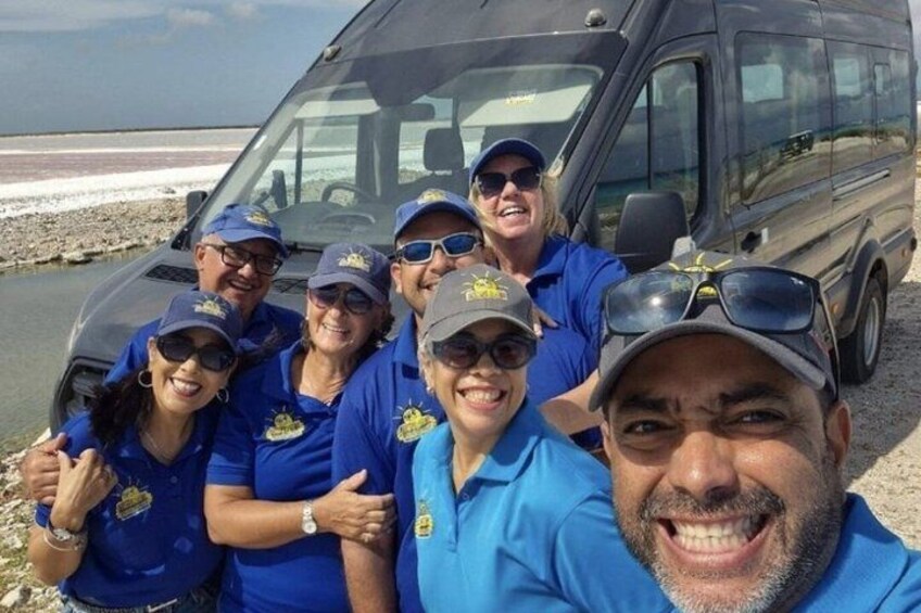 Un grupo de personas con camisetas y gorras azules posando frente a una camioneta negra en la playa. 2