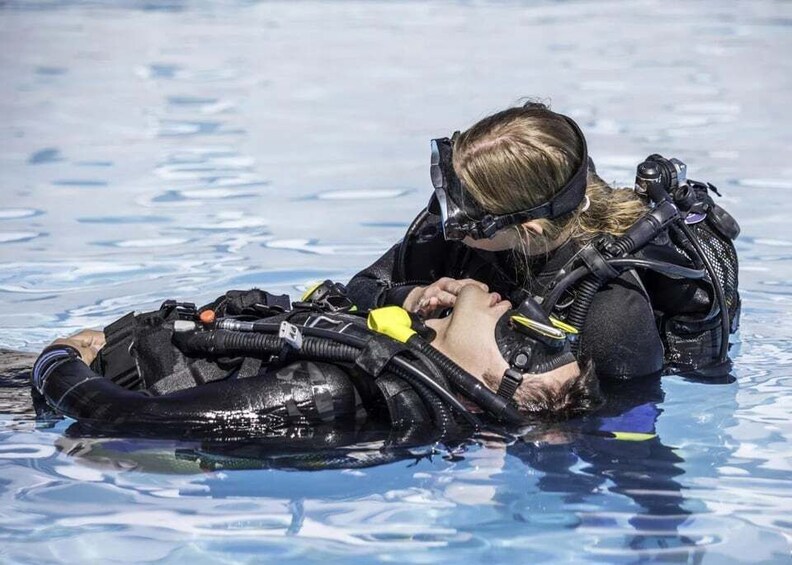 A person in a black wetsuit and scuba gear assisting another person in a pool. 5