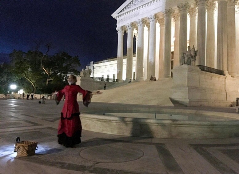 A person in a red dress standing in front of a neoclassical building with columns at night. 3