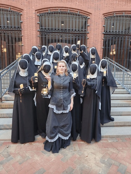 A group of people in nun habits standing on steps in front of a brick building with barred windows. 1