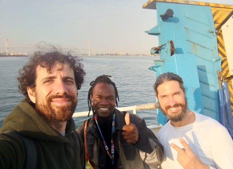Three people on a boat with a blue structure and a bridge in the background. 2