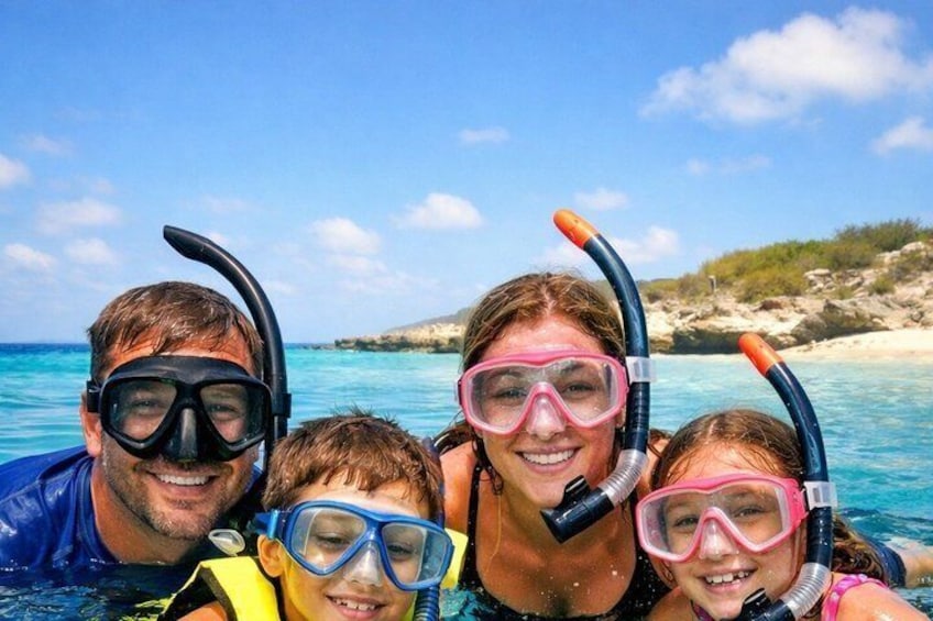Una familia practica snorkel en aguas azul turquesa con una playa rocosa al fondo. 1