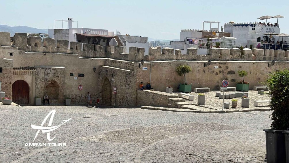 A historic stone wall with a gate, a café, and a view of the city. 2