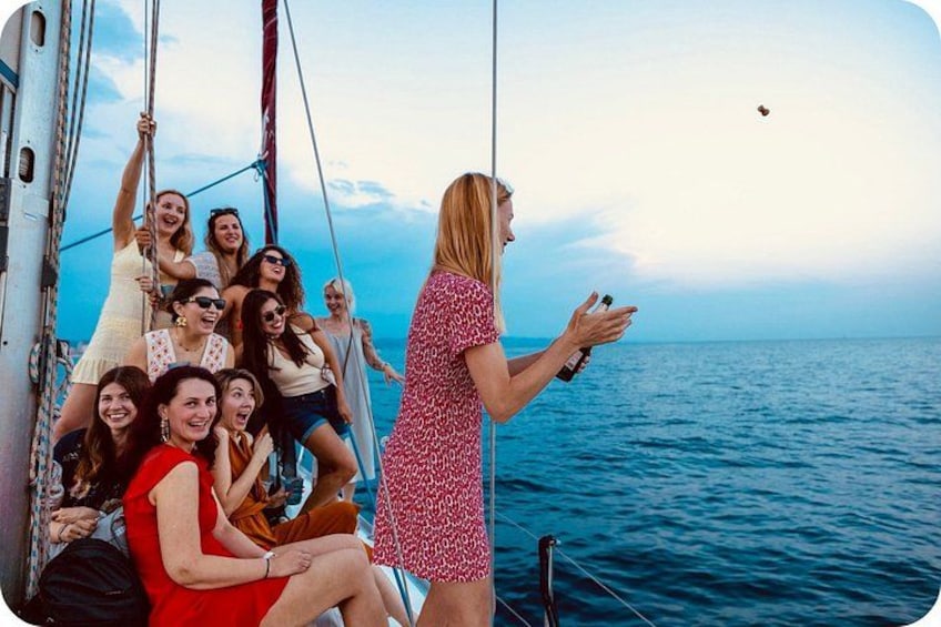 A group of people on a sailboat with a woman holding a bottle. 5