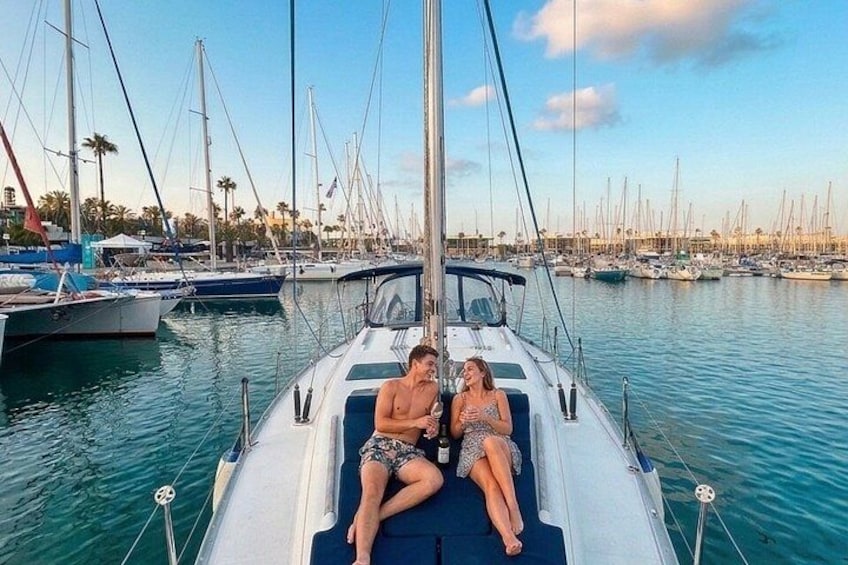 A couple on a sailboat in a marina with multiple boats and palm trees in the background. 3