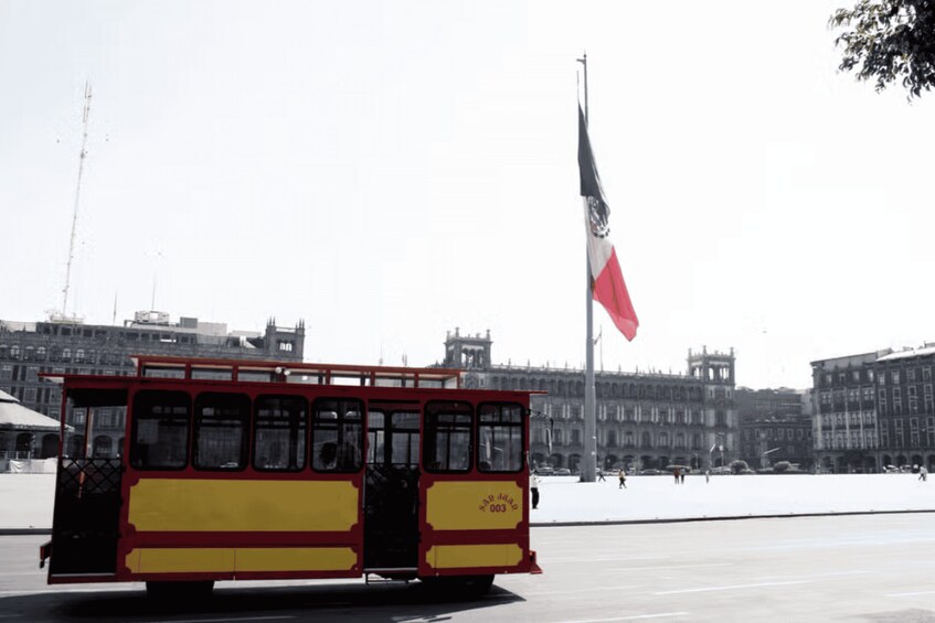 A red and yellow tram in a square with a flagpole and historic buildings in the background. 3
