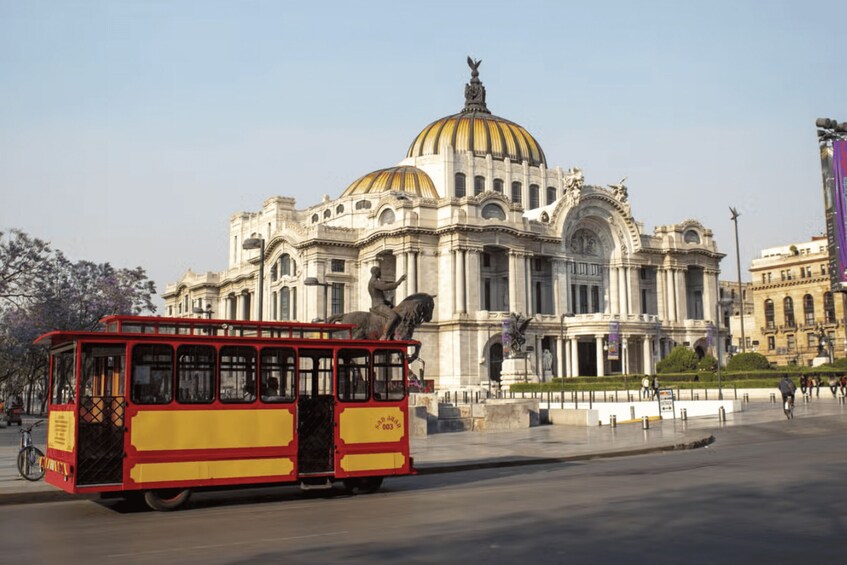A red and yellow tram in front of a large, ornate building with a golden dome. 2