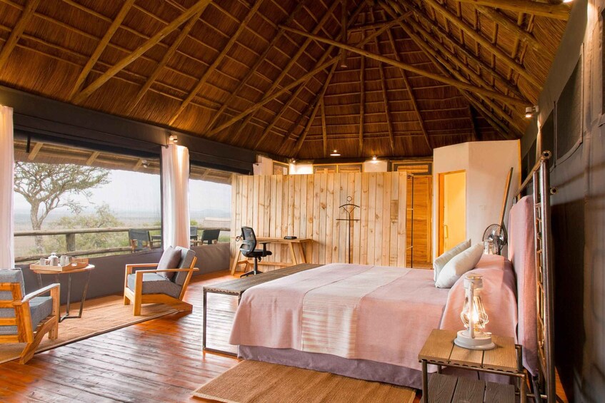 A cozy bedroom with a wooden ceiling, a large bed, a desk, and a chair. 1