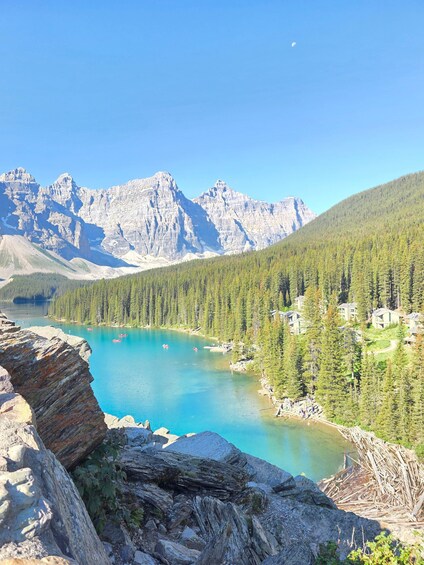 A mountainous landscape with a turquoise lake, dense forest, and a small settlement. 2