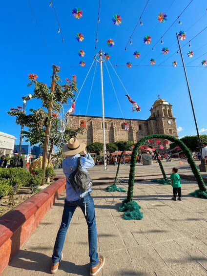 A person taking a photo of a plaza with a historic building and colorful decorations. 5