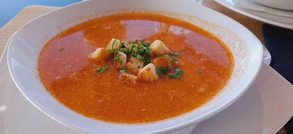 A bowl of tomato soup garnished with croutons and herbs. 5
