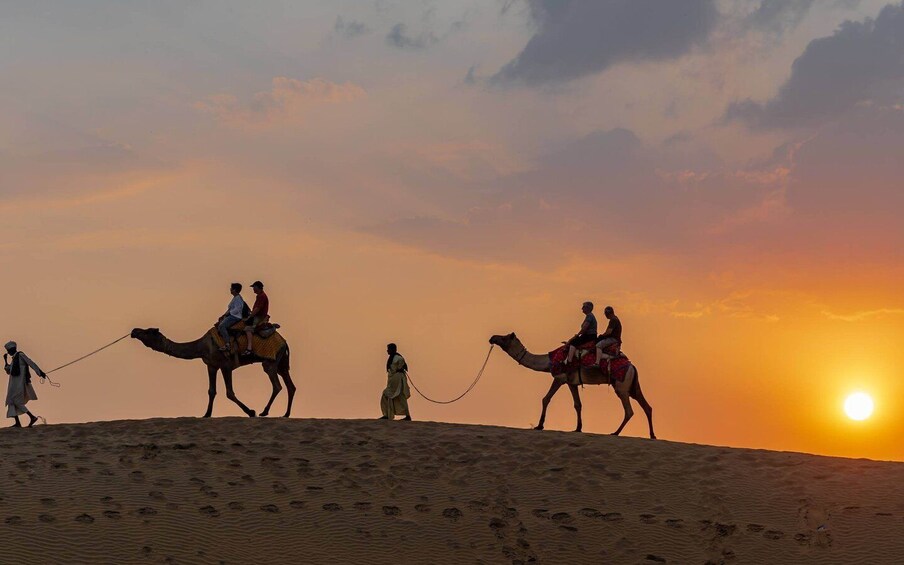 A camel caravan at sunset with people riding camels. 5