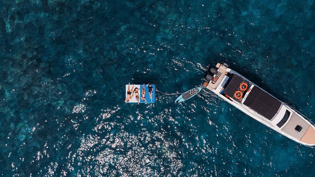 A boat towing a floating platform with people on it. 3