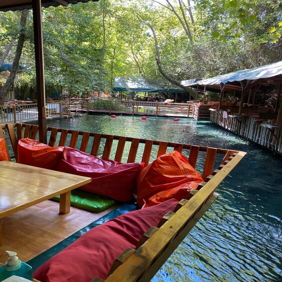 A wooden boat with colorful cushions and a table, surrounded by a calm water body with a wooden walkway and trees in the background. 5