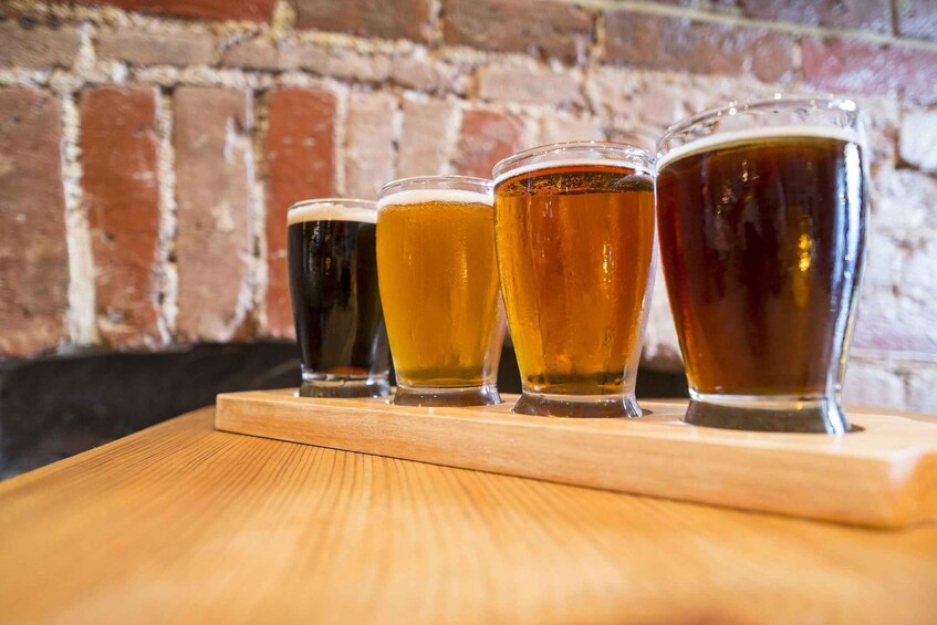 Four glasses of beer on a wooden board against a brick wall. 4