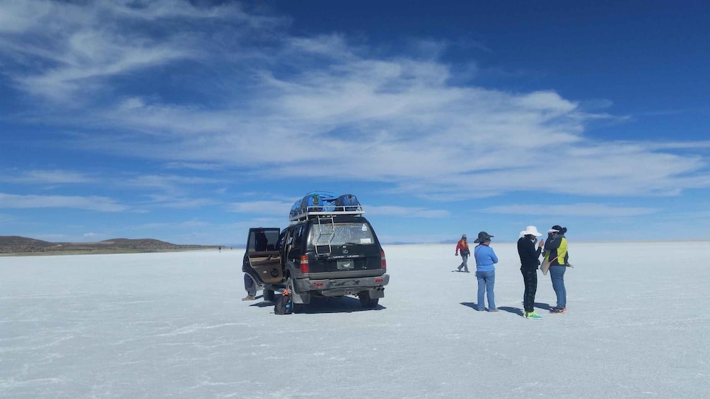 A black SUV with a roof rack parked on a salt flat under a clear sky. 1