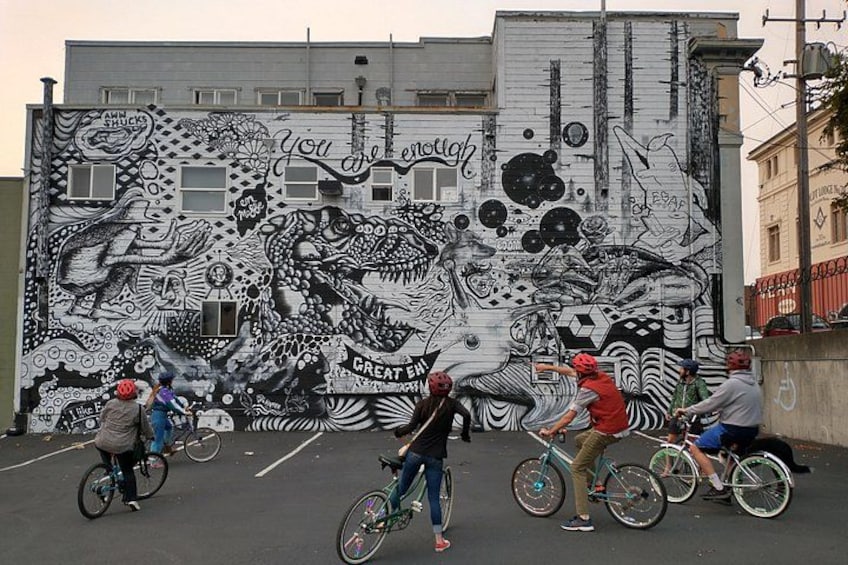A mural with a bicycle and people riding bikes in front of it. 1