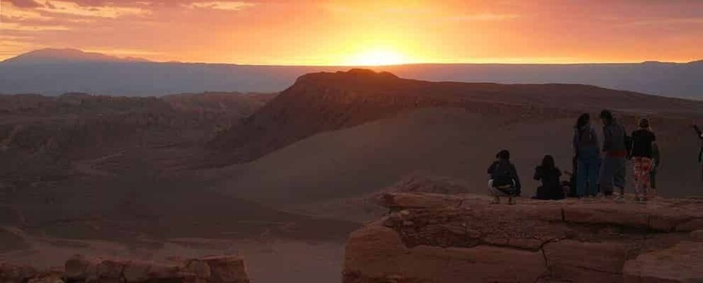 Un groupe de personnes se tient sur un promontoire rocheux, d’où elles dominent un vaste canyon, au moment du coucher du soleil. 5