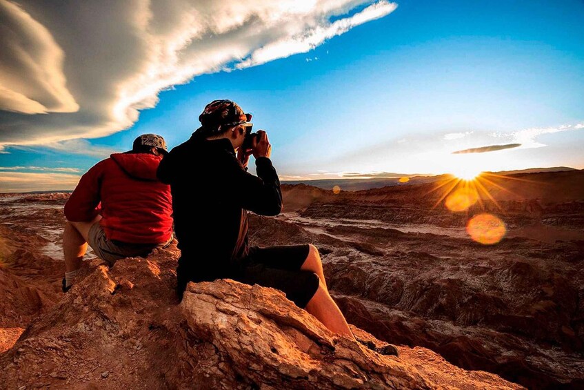 Deux personnes assises sur des rochers, prenant des photos du coucher de soleil. 3
