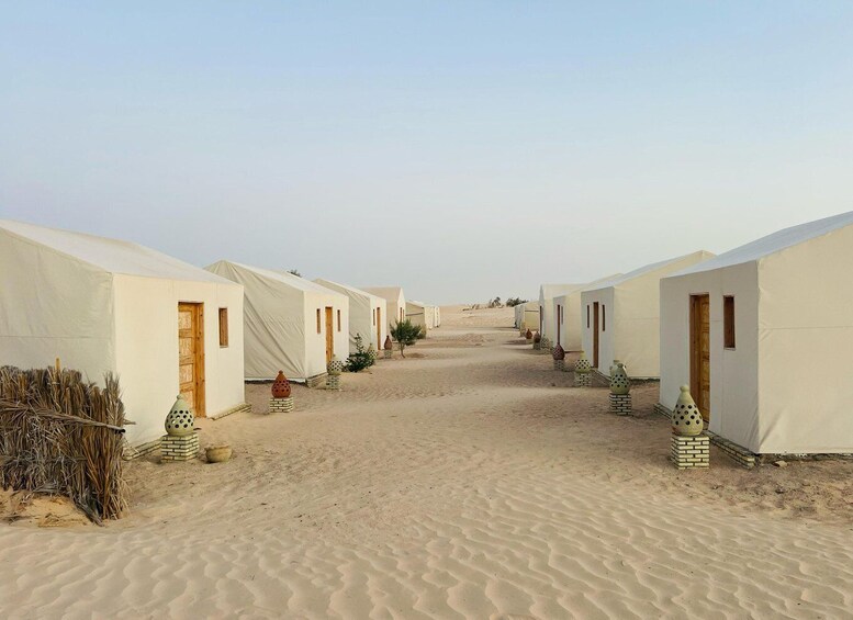 A row of white tents with wooden doors, set in a desert landscape. 3