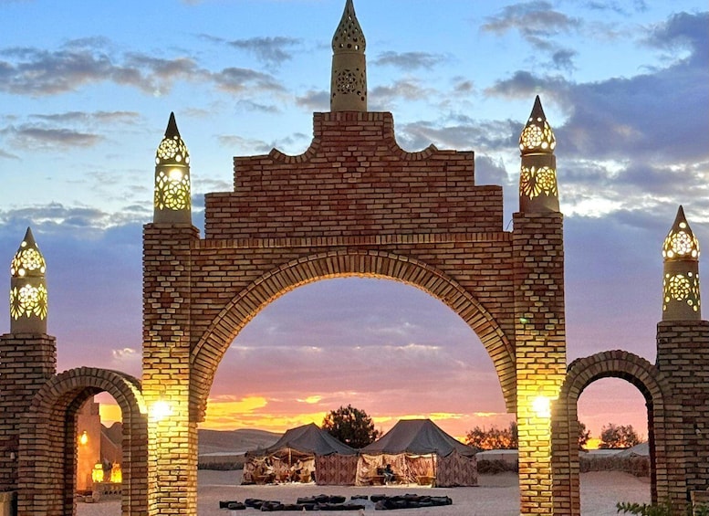 A brick archway with pointed tops and decorative lights, leading to a campsite with tents. 1