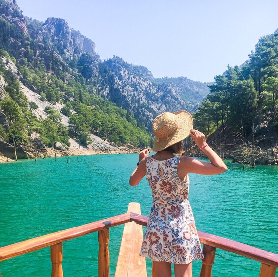 A person on a wooden pier overlooking a turquoise lake with a mountainous backdrop. 4