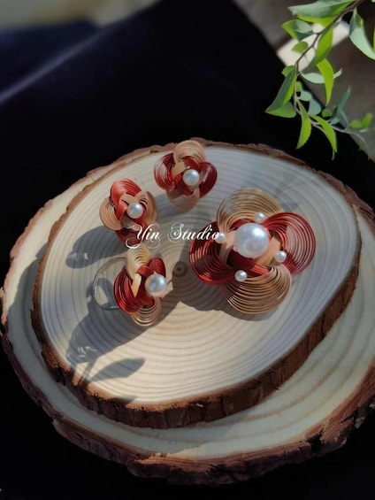 A wooden slice with red and beige coiled wire sculptures and pearls, labeled "Yin Studio". 2