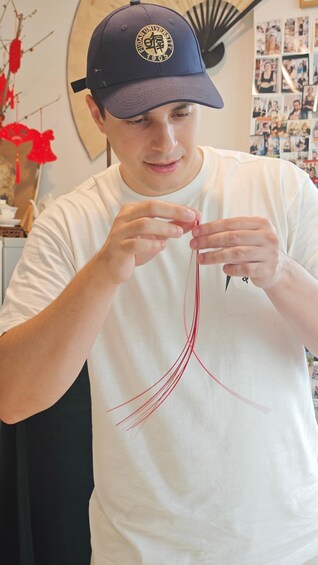 A person wearing a cap and a white t-shirt, holding a red thread. 1