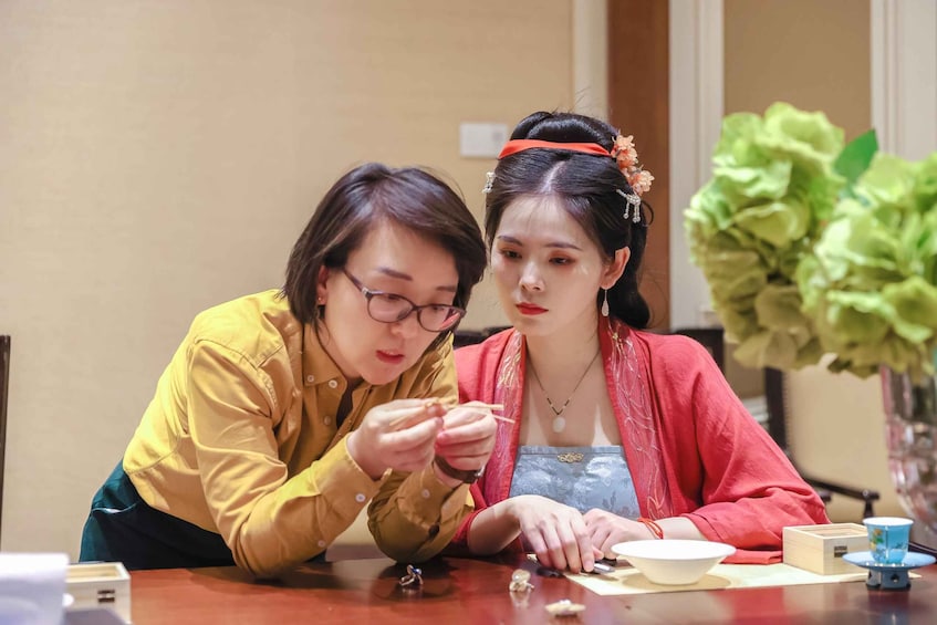 Two people sitting at a table, one holding a spoon and the other looking at a bowl. 1